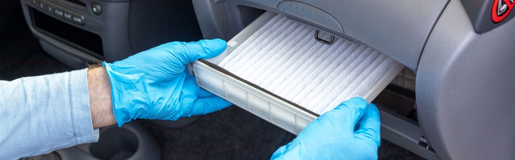 A person replacing the cabin air filter in a car's glove compartment while wearing blue gloves.

