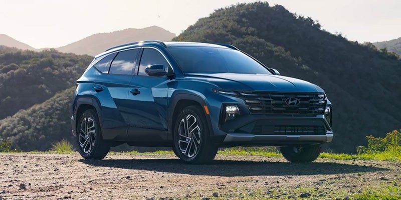 Blue Hyundai Tucson SUV parked on a mountain road with a scenic background.
